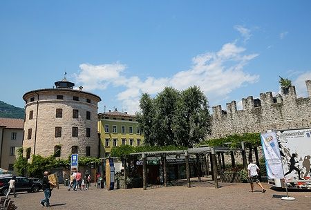 Vista di Piazza Di Fiera a Trento con torre e mura medievali sotto cielo blu.