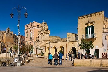 Piazza Vittorio Veneto a Matera con chiese e persone sotto un cielo blu.