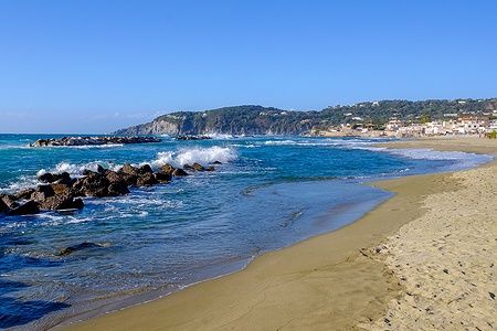 Spiaggia di Chiaia a Ischia con sabbia, mare e scogli sotto un cielo azzurro.