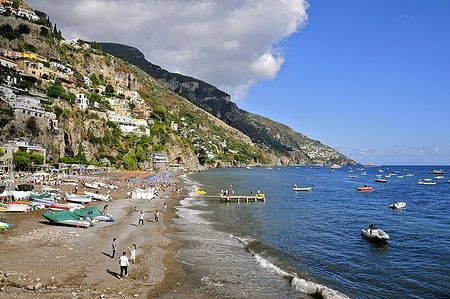 Spiaggia affollata a Positano con case colorate sulla collina e barche in mare.