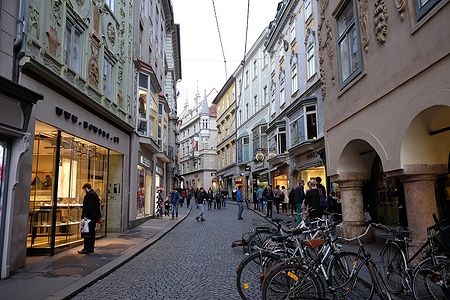 Biciclette parcheggiate in una strada di Sporgasse, Graz, con persone che passeggiano.