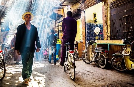 Strada affollata nella Medina di Marrakech con persone e biciclette.