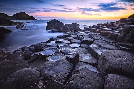 Tramonto sul Giant's Causeway con rocce basaltiche in primo piano.