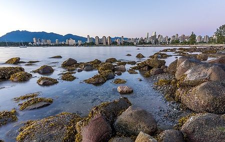 Skyline di Vancouver all'ora blu visto dalla spiaggia di Kitsilano con rocce in primo piano.