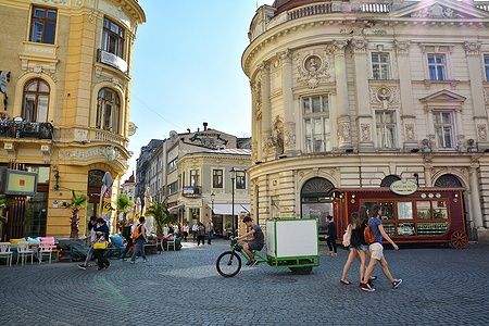 Persone passeggiano nella vivace vecchia città di Bucarest, tra edifici storici e bar.