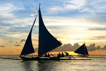 Barca a bilanciere con turisti al tramonto a Boracay, Filippine.