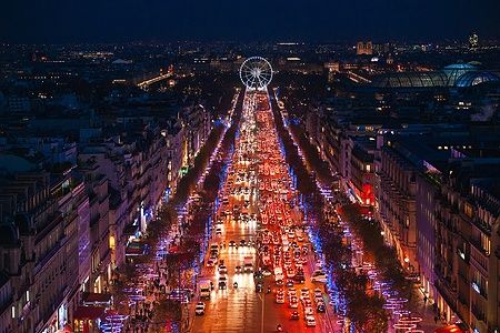Vista notturna dei Champs-Élysées illuminati a Parigi, con traffico e ruota panoramica in lontananza.