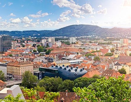 Vista di Graz con il museo Kunsthaus e tetti rossi sotto un cielo blu.
