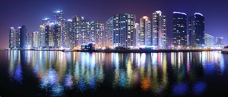 Grattacieli illuminati di notte nel distretto di Haeundae, Busan, riflessi sull'acqua.