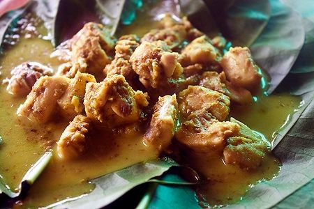 Piatto di Lok Lak cambogiano su foglie verdi con pezzi di carne in salsa.