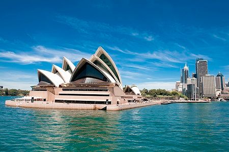 Sydney Opera House con vele bianche sullo sfondo del cielo azzurro e del porto.