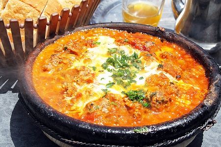 Tajine marocchino con carne, verdure e polpette in piatto di terracotta.