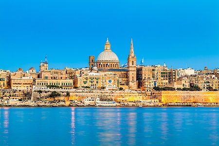 Skyline di Valletta, Malta, con Basilica e Cattedrale illuminate di sera.