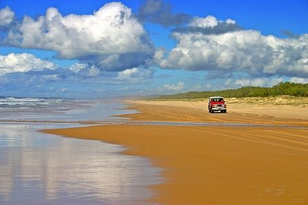 Jeep rossa su Fraser Island in Australia con cielo blu e nuvole.