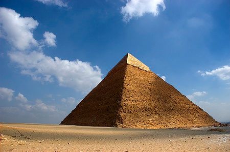 La Grande Piramide di Cheope a Giza sotto un cielo azzurro con nuvole.