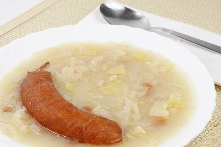 Jota tradizionale slovena con salsiccia in un piatto bianco.