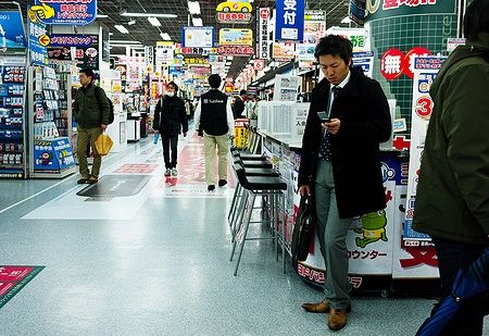 Uomo in un negozio di Akihabara a Tokyo con molti cartelli colorati.