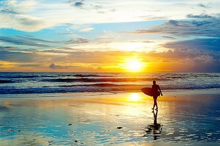 Surfista sulla spiaggia al tramonto a Bali, Indonesia.