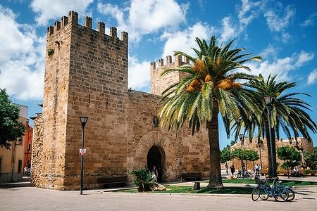 Porta delle mura storiche di Alcudia con palme e cielo azzurro.