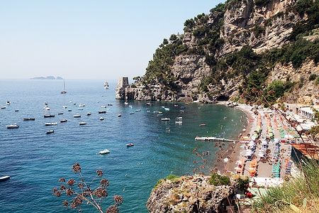 Spiaggia di Fornillo a Positano con mare azzurro e ombrelloni colorati.