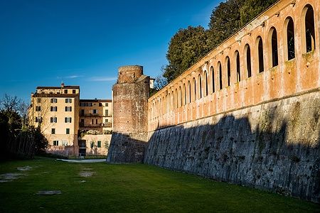 Mura medievali del Giardino Scotto a Pisa con un prato verde e cielo sereno.