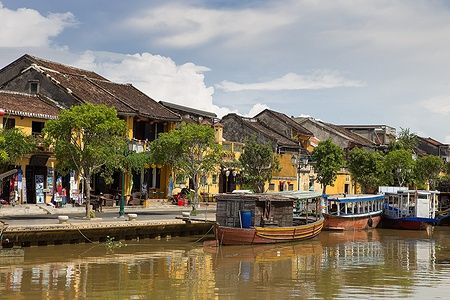 Barche di legno sul Fiume Thu Bon a Hoi An con case gialle storiche.