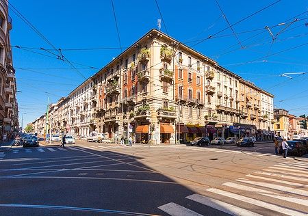 Persone su un attraversamento pedonale a Corso Buenos Aires, Milano, con edifici storici.