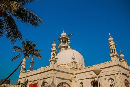 Vista della Moschea Haji Ali a Mumbai con cielo blu e palma.