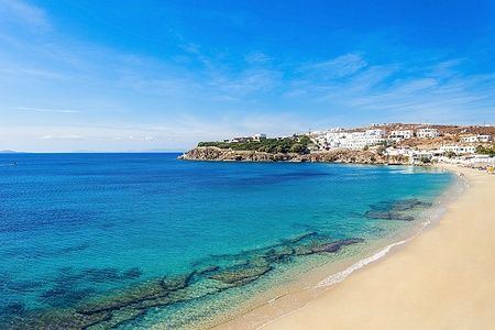 Spiaggia di Agios Stefanos a Mykonos, Grecia, con mare azzurro e sabbia dorata.