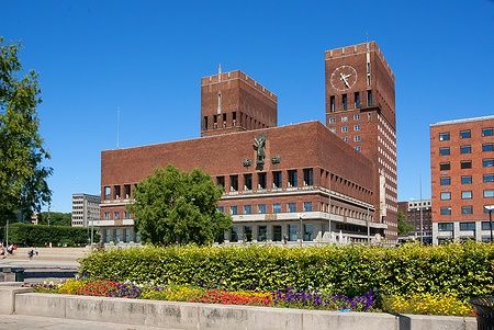 Il municipio di Oslo con cielo azzurro e fiori davanti.