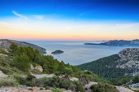 Vista panoramica di Port de Pollença al tramonto con mare e colline.