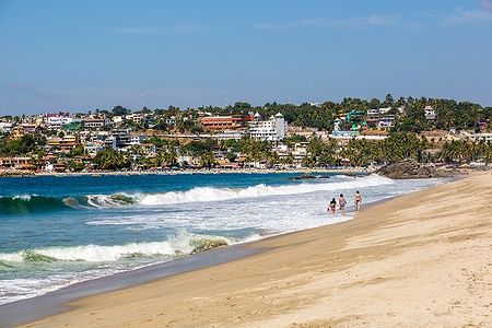 Persone camminano sulla spiaggia di Puerto Escondido, Messico con foresta sullo sfondo.