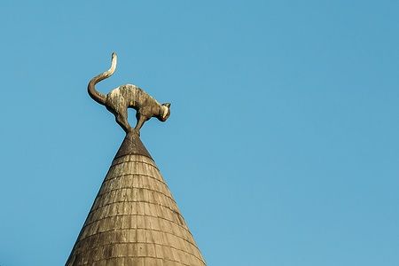 Scultura di gatto nero sulla torretta del Cat House a Riga, su sfondo di cielo blu.