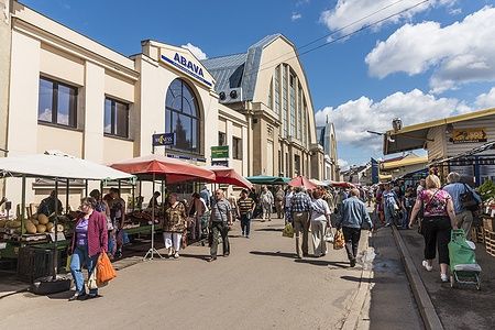 Scene di mercato al Riga Central Market con persone e bancarelle colorate.