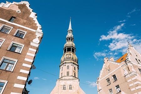 Guglia con orologio della Chiesa di San Pietro a Riga tra edifici storici.