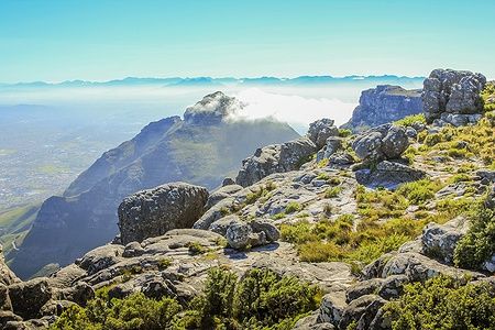 Vista di Table Mountain con nuvole basse e rocce in primo piano nel parco nazionale.