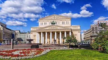 Facciata del Teatro Bolshoi a Mosca, con giardino fiorito e cielo blu.