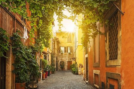 Una strada acciottolata nel quartiere di Trastevere a Roma con edifici colorati e piante rampicanti.
