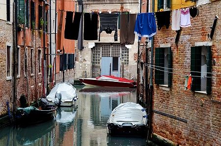 Canale nel ghetto ebraico di Venezia con panni stesi e barche coperte.