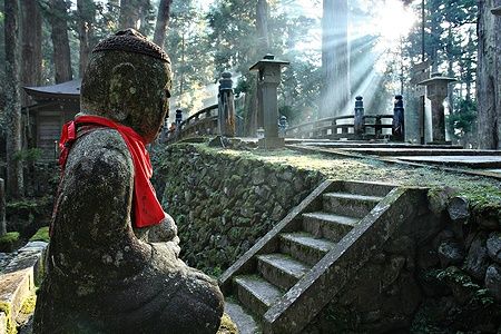Statua di Buddha nel cimitero di Okunoin, Monte Koya, con raggi solari tra gli alberi.