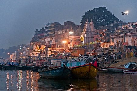 Vista notturna di Varanasi dal fiume Gange con edifici illuminati e barche.