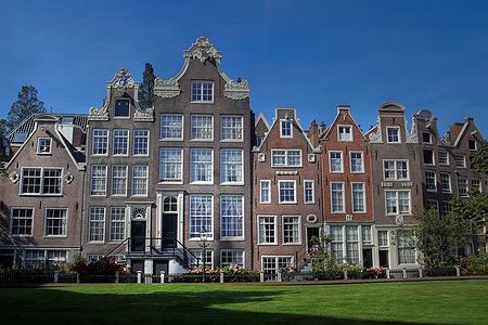 Case storiche del Begijnhof ad Amsterdam con giardino e cielo blu.