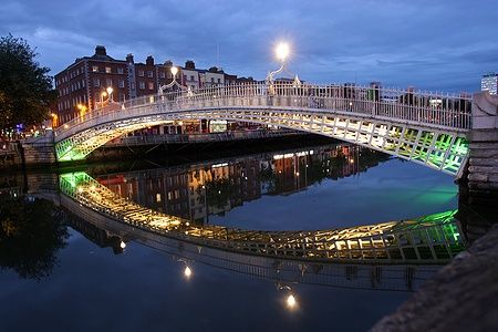 Il Ha'penny Bridge illuminato di notte a Dublino, riflesso nel fiume.
