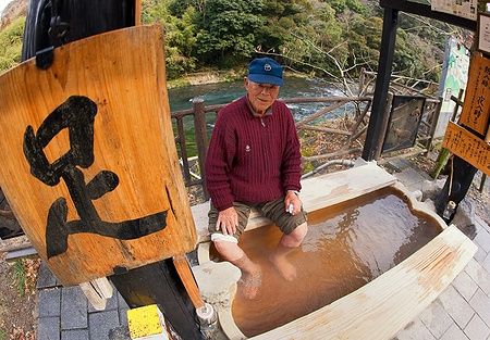 Uomo anziano giapponese che immerge i piedi in una sorgente termale a Kirishima.