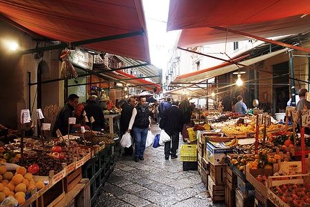 Mercato del Capo a Palermo con bancarelle di frutta e verdura e persone che passeggiano.