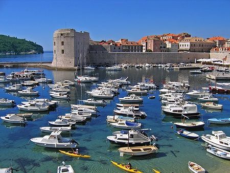 Il porto di Dubrovnik con tante barche e kayak sull'acqua, circondato da mura antiche.