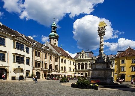 Piazza principale di Sopron, Ungheria, con edifici storici e monumento centrale.