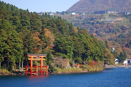 Un torii rosso sul Lago Ashi in Giappone, circondato da alberi.
