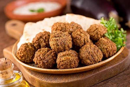 Falafel serviti con pane pita e prezzemolo su un vassoio di legno.
