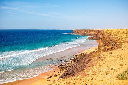 Costa rocciosa e sabbiosa a Fuerteventura, vicino a El Cotillo, sotto un cielo sereno.